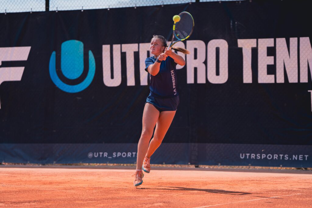 A player hitting a two-handed backhand in front of the UTR Pro Tennis banner during the Showcase.