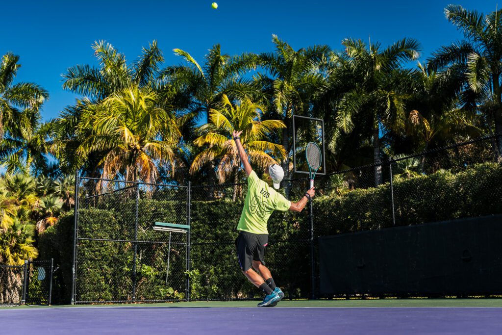 Player serving on a tennis court surrounded by palm trees in Florida
