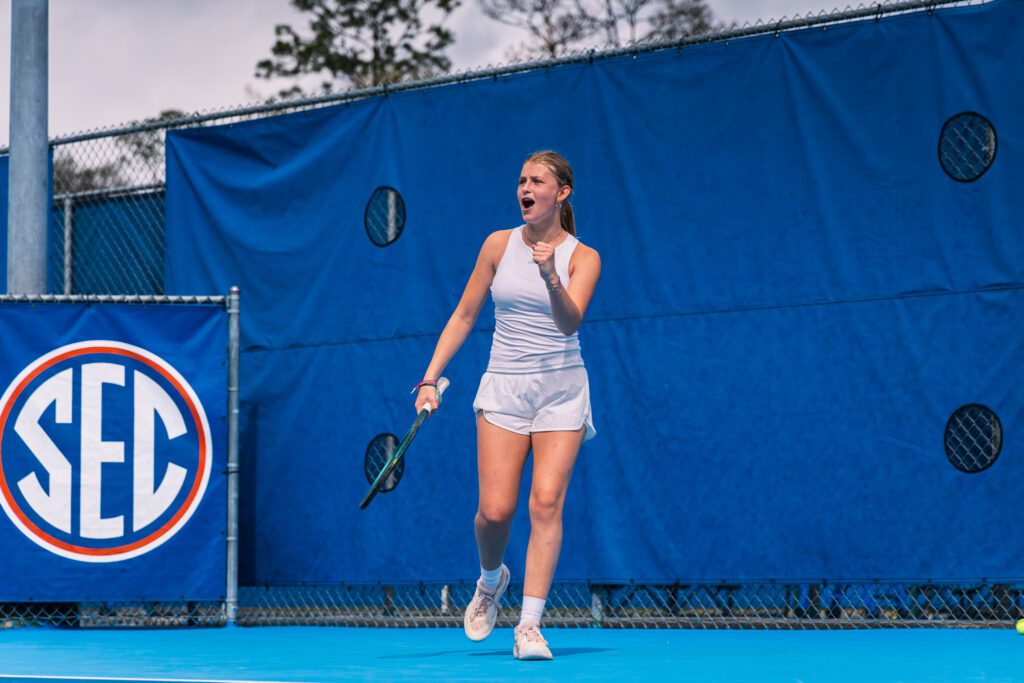 College tennis player celebrating a point in front of the SEC logo in Florida